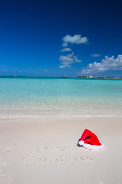 メリー クリスマス クリスマス帽子と熱帯のビーチの白い砂に書かれました。 — ストック写真