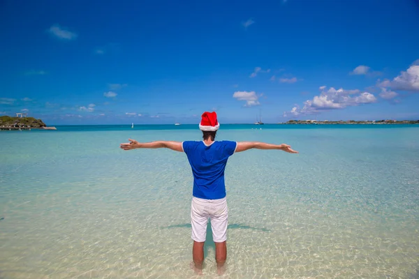 Vista posteriore del giovane uomo in cappello di Babbo Natale sulla spiaggia tropicale — Foto Stock