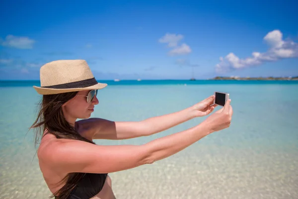 年轻女子在她的手机在地处热带的海滩上拍张照片 — 图库照片