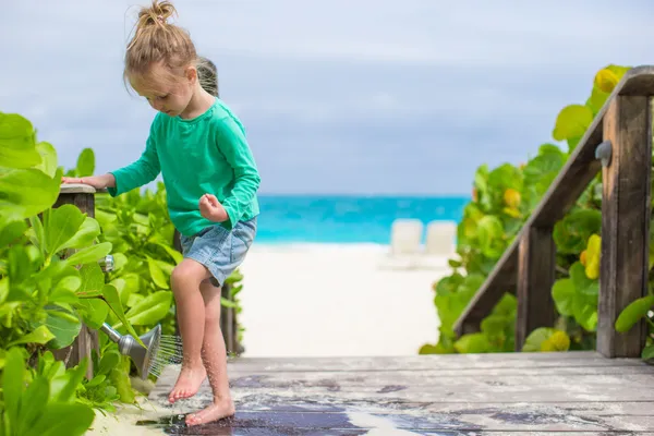 Piccola ragazza carina lava la sabbia dai suoi piedi sulla spiaggia tropicale — Foto Stock