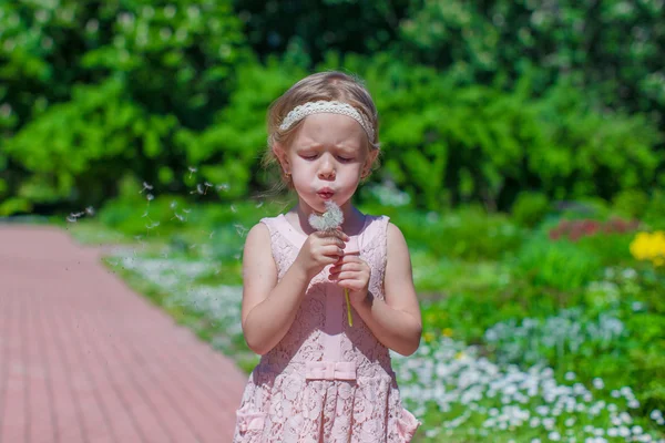 Portrett av en søt liten jente som blåser løvetann i parken – stockfoto