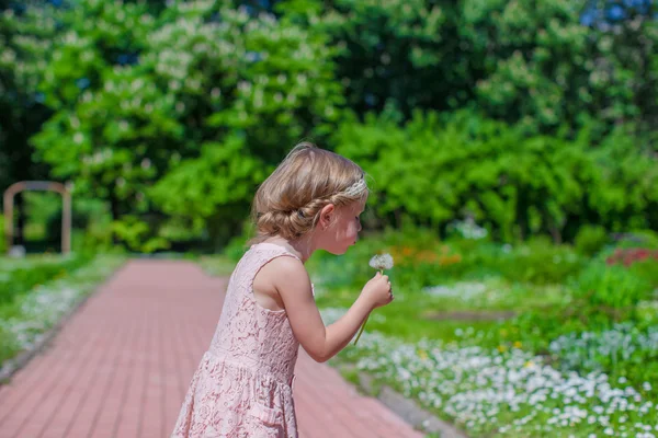 Glad liten tjej som blåser en maskros i blommande park — Stockfoto