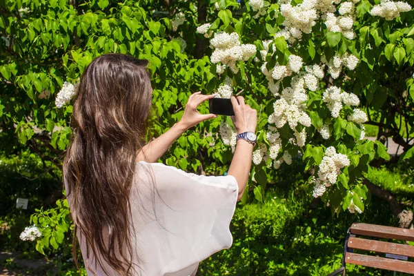 Ung kvinna ta ett foto av sin phonr i lila trädgård — Stockfoto