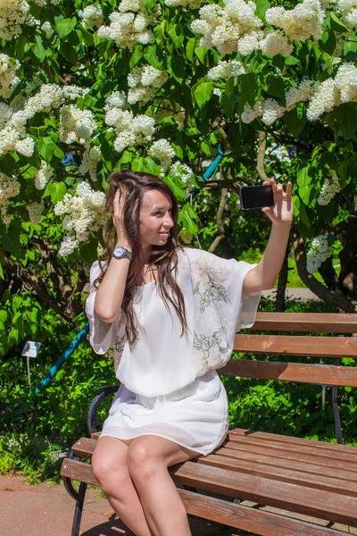 Young woman take photo on her phone at blossoming lilac garden — Stock Photo, Image