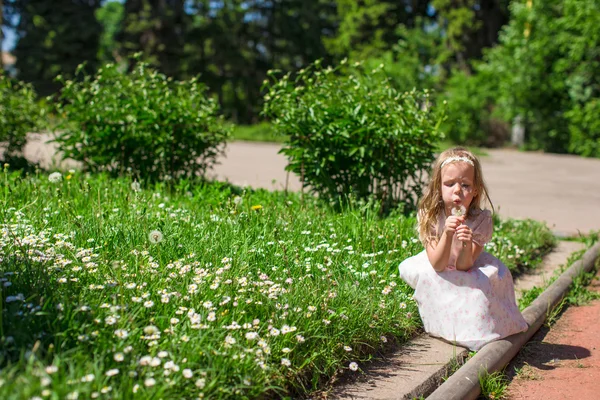 Bedårande liten flicka blåser en maskros i parken — Stockfoto