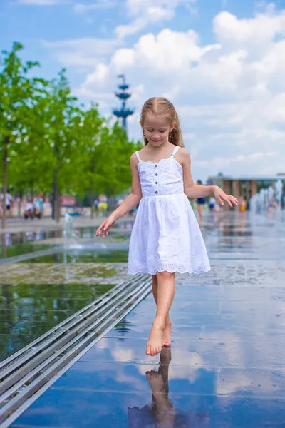 Маленькая милая девочка ходит в фонтан на открытой улице в жаркий солнечный день — стоковое фото
