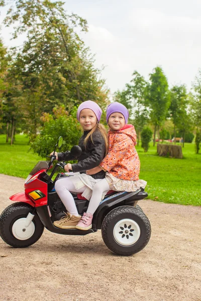 Adorable little girls riding on kid's motobike in the green park — Stock Photo, Image