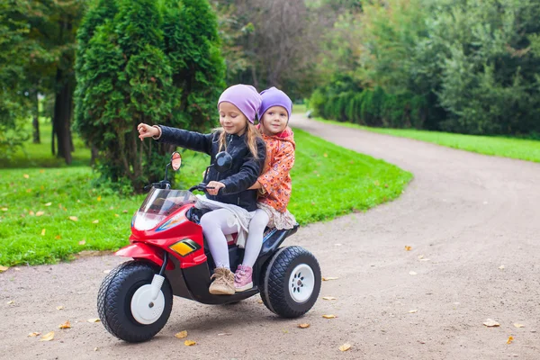 Adorables niñas montando en moto de niño en el parque verde —  Fotos de Stock