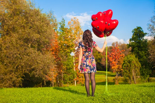 Vista posteriore della giovane ragazza con palloncini rossi sorridenti in mano all'aperto — Foto Stock