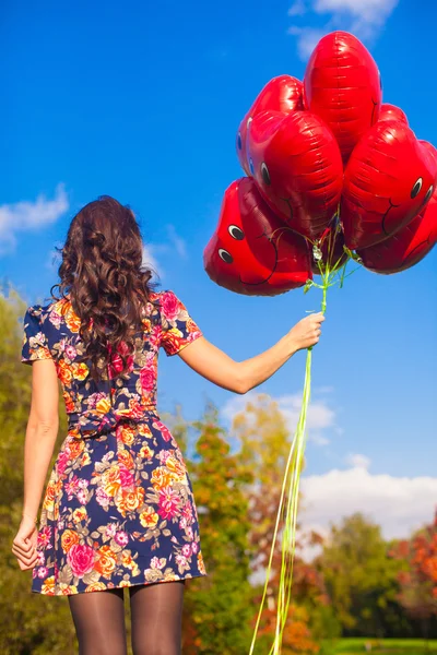 Back view of young girl with red smiling balloons in hand outdoor — Stock Photo, Image