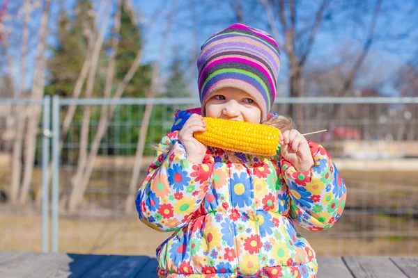 Little adorable girl eating corn in the park on warm spring day — Stock Photo, Image