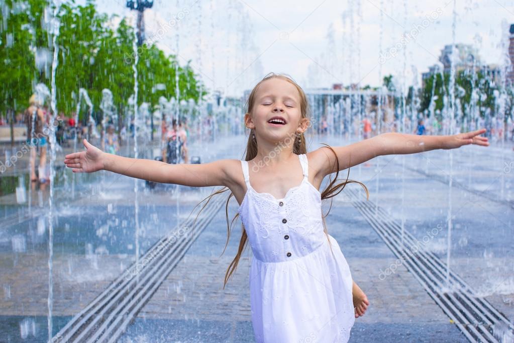 Portrait of little happy girl have fun in street fountain at hot sunny day