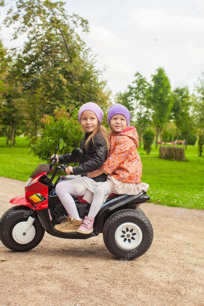 Adorable little girls riding on kid's motobike in the green park