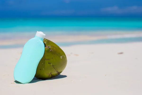 Coconut and suncream on white sandy beach — Stock Photo, Image