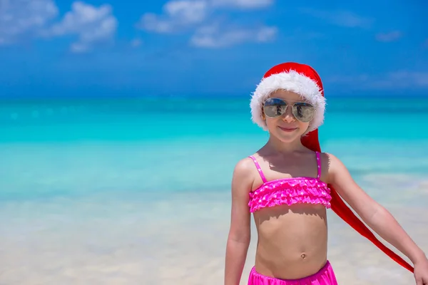 Urocze dziewczynki w czerwonym kapeluszu santa na tropikalnej plaży — Zdjęcie stockowe