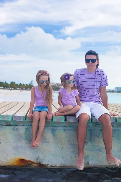 Семья из трех человек сидит на деревянном причале и наслаждается видом на океан — стоковое фото