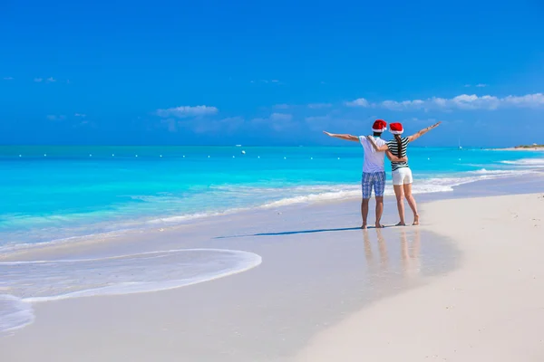 Vista trasera de pareja joven en sombreros rojos de Santa en la playa de arena tropical — Foto de Stock