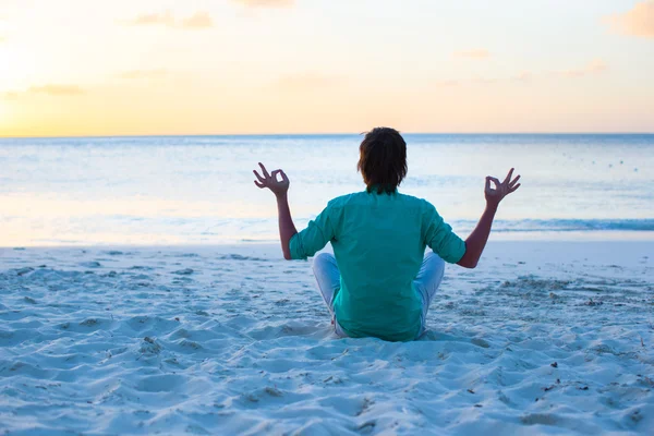 Jonge man zit in de lotuspositie op wit zand strand — Stockfoto