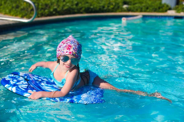 Little girl swimming on a surfboard in swimmingpoll — Stock Photo, Image