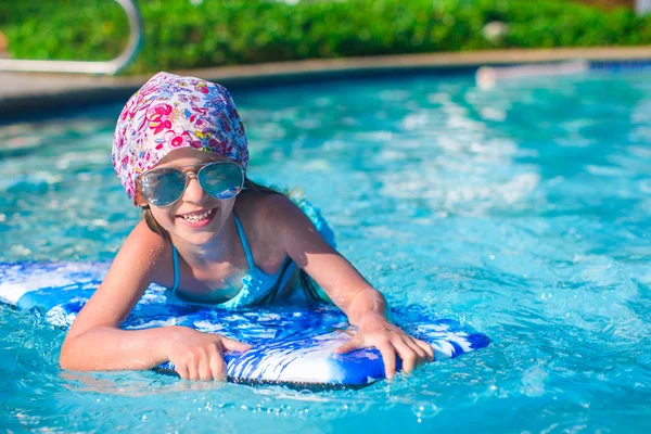 Klein meisje zwemmen op een surfplank in swimmingpoll — Stockfoto