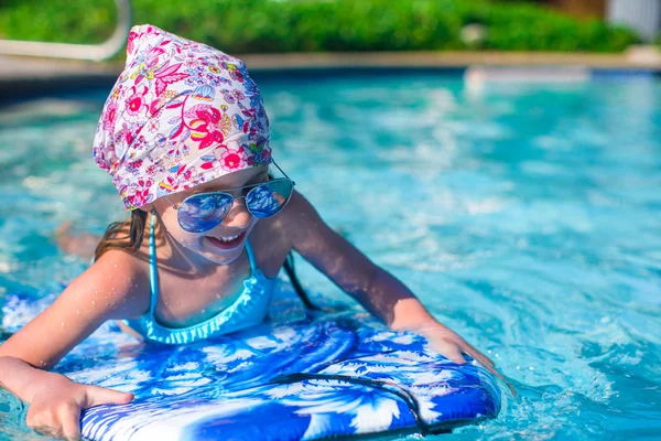 Little girl swimming on a surfboard in swimmingpoll — Stock Photo, Image