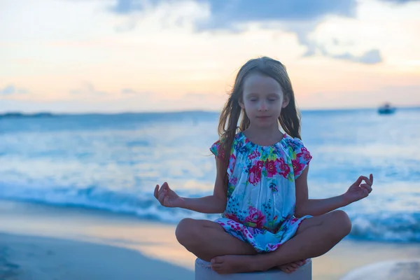 Beautiful little girl sitting in a lotus position on an exotic beach — Stock Photo, Image