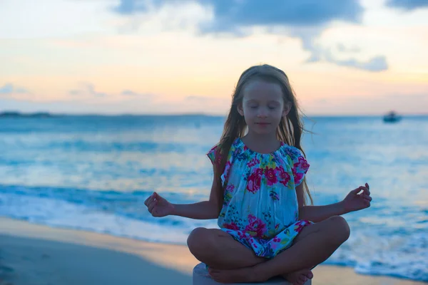 Beautiful little girl sitting in a lotus position on an exotic beach — Stock Photo, Image