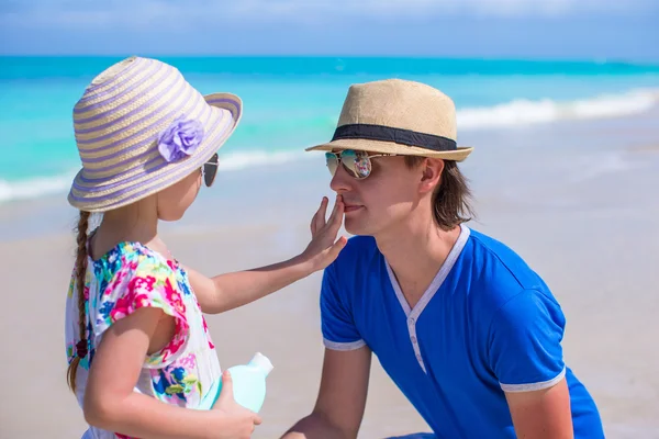 Маленька дівчинка отримує сонячний крем на носі своїх батьків — стокове фото