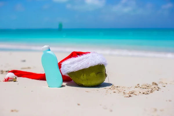 Suncream and Santa Hat on coconut at white exotic beach — Stock Photo, Image