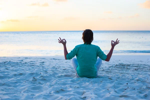 Young man sitting in the lotus position on white sand beach — Stock Photo, Image