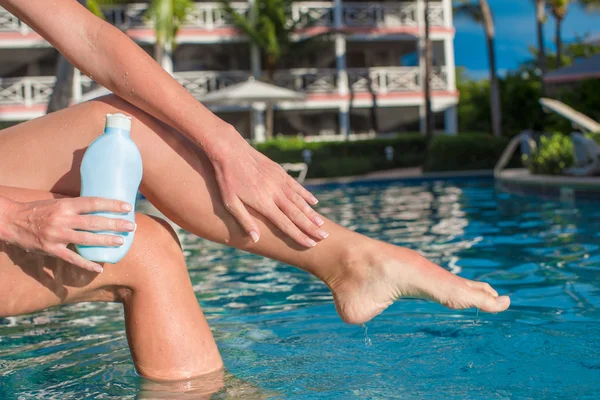 晒得黑黑的女性双腿靠近游泳池和防晒霜 — 图库照片