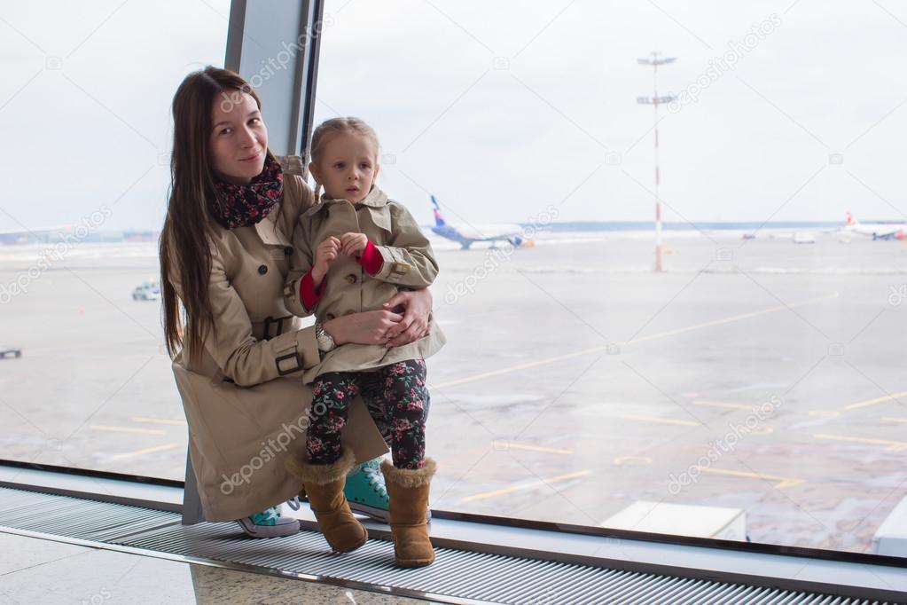 Mother and little daughter looking out the window at airport terminal