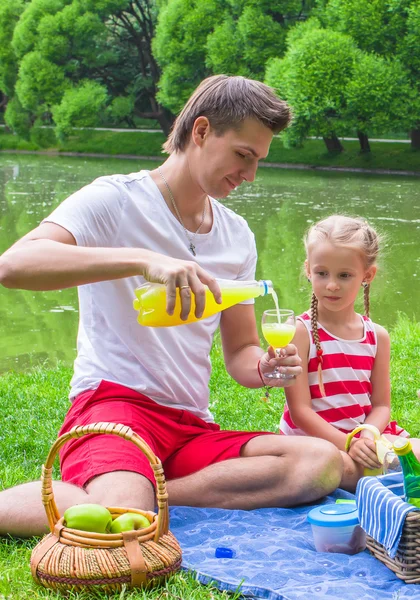 Padre joven con niña tienen picnic al aire libre y beber jugo —  Fotos de Stock