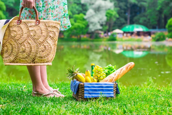 Корзина для пикника с фруктами, хлебом и шляпой на соломенной сумке — стоковое фото