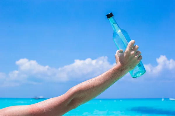 Fles met een bericht in de hand achtergrond blauwe hemel — Stockfoto