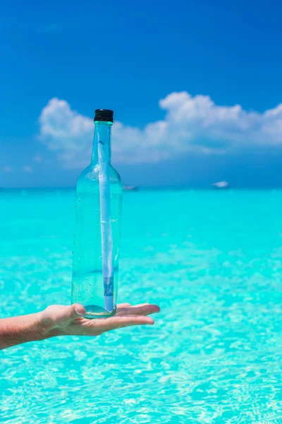 Flaska med ett meddelande i hand bakgrunden blå himlen — Stockfoto