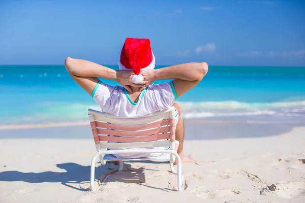 Achteraanzicht van jonge man in Kerstman hoed ontspannen in strandstoel — Stockfoto