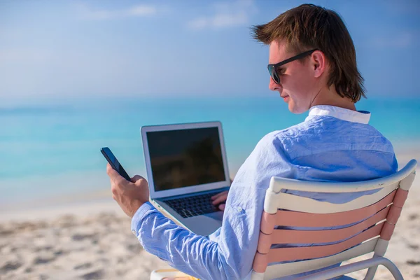 Ung forretningsmand ved hjælp af bærbar computer på tropisk strand - Stock-foto