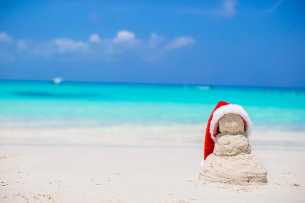 Kleine zandige sneeuwpop met rode kerstmuts op witte Caribisch strand — Stockfoto