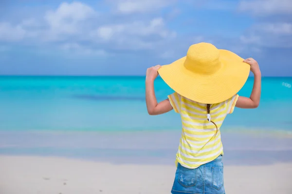 Rear view of little girl in a big yellow straw hat on white sand beach — Stock Photo, Image