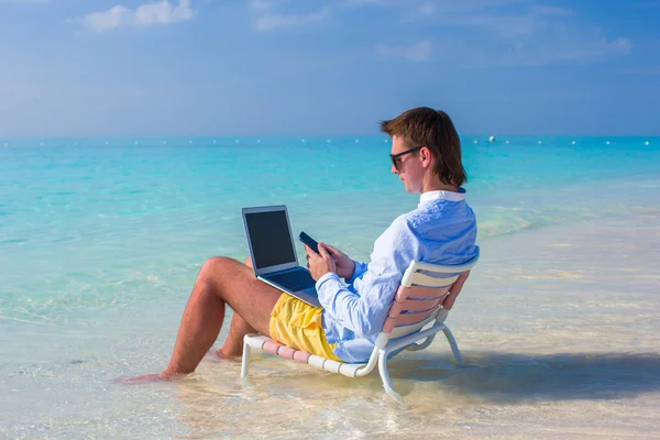 Giovane uomo che utilizza il computer portatile sulla spiaggia tropicale — Foto Stock
