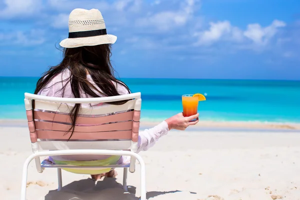 Tillbaka Visa ung långhåriga kvinna med cocktail i handen och halm hat på stranden — Stockfoto