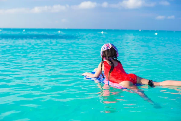 Kleines süßes Mädchen schwimmt auf einem Surfbrett im türkisfarbenen Meer — Stockfoto