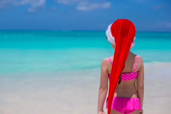 Vista trasera de linda chica en el sombrero rojo de santa claus en la playa —  Fotos de Stock