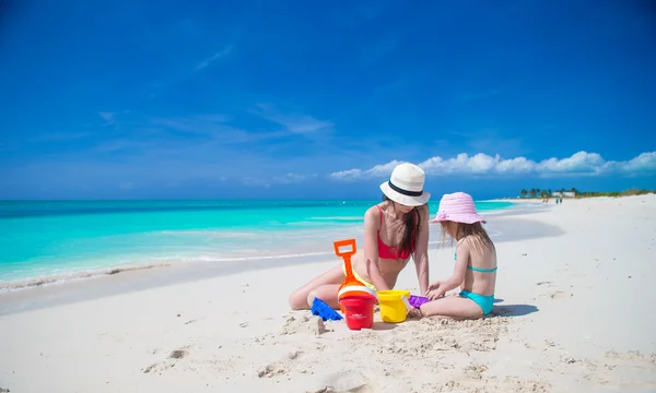 Маленькая милая девочка и молодая мать строят песчаный замок на тропическом пляже — стоковое фото