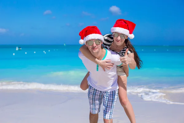 Young happy couple in red Santa hats on white beach — Stock Photo, Image