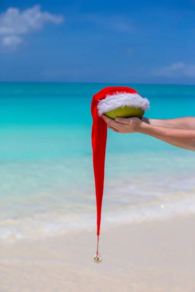 Coco com chapéu de Papai Noel em mãos masculinas contra o mar turquesa — Fotografia de Stock