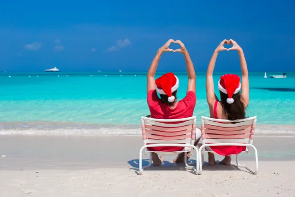 Feliz casal romântico em vermelho Santa Chapéus na praia fazendo corações — Fotografia de Stock