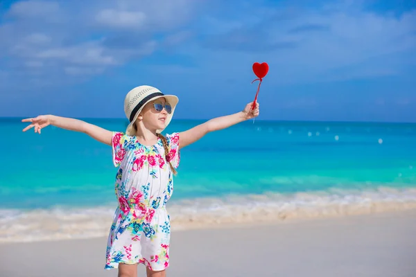 Маленькая счастливая девочка с красным сердцем в руках на тропическом пляже — стоковое фото