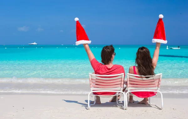 Feliz pareja joven en Santa Sombreros rojos sentados en sillas de playa —  Fotos de Stock